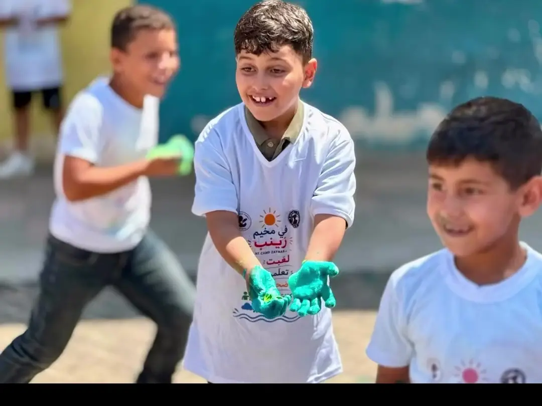 A child showing paint-covered hands during a Camp Zaynab activity