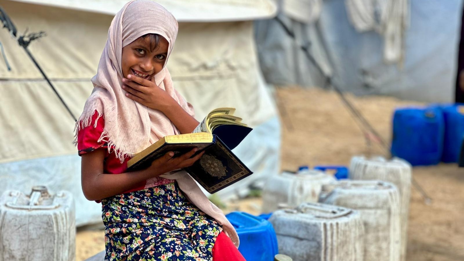 A girl reading beside water containers in an official Zaynab Project campaign photograph