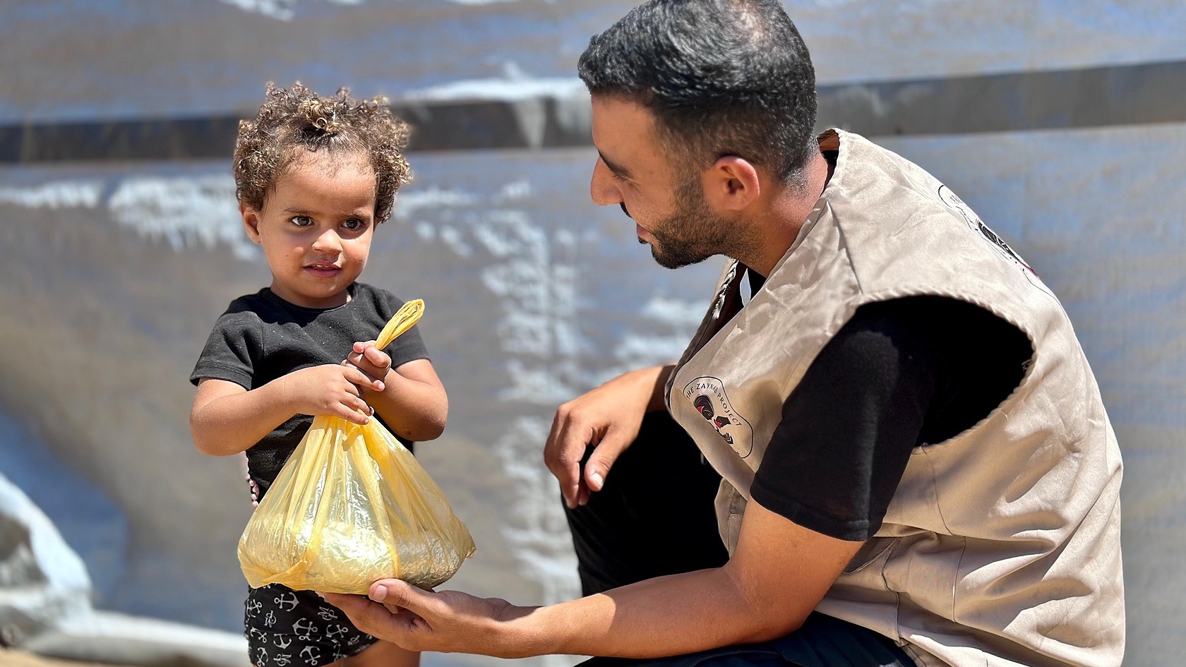 A Zaynab Project team member crouching while offering a small bag to a young child